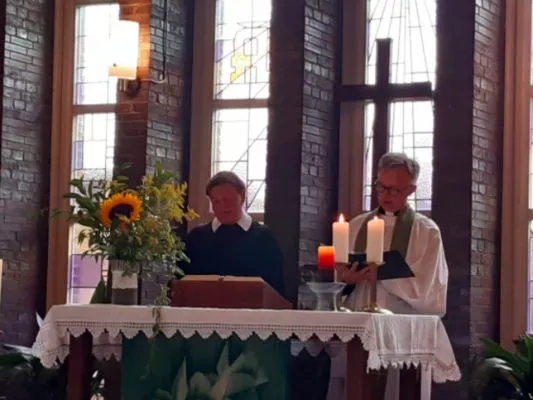 Zwei Geistliche am Altar mit brennender Partnerkerze und Blumenschmuck